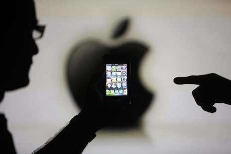 Men are silhouetted against a video screen with an Apple logo as they pose with an Apple iPhone 4 smartphone in this photo illustration take Men are silhouetted against a video screen with an Apple logo as they pose with an Apple iPhone 4 smartphone in this photo illustration take