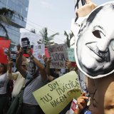 People protest holding masks printed with the face of Mexican telecommunications and retail tycoon Carlos Slim as he attends the Meeting of 