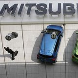 Mitsubishi Motors Corp's vehicles and a passer-by are reflected on an external wall at the company headquarters in Tokyo April 25, 2013. REU