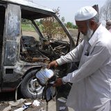 A man displays a burnt book to the media near a burnt-out school bus on the outskirts of Gujrat, 100 miles (170 km) southeast of Islamabad, 
