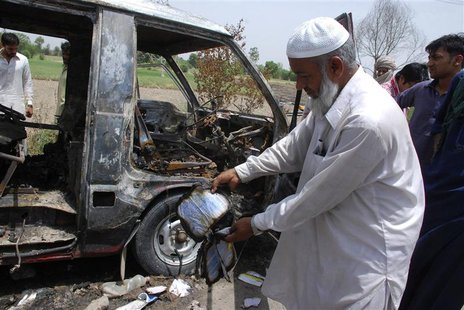 A man displays a burnt book to the media near a burnt-out school bus on the outskirts of Gujrat, 100 miles (170 km) southeast of Islamabad, A man displays a burnt book to the media near a burnt-out school bus on the outskirts of Gujrat, 100 miles (170 km) southeast of Islamabad,