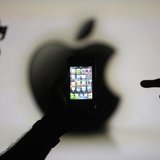 Men are silhouetted against a video screen with an Apple logo as they pose with an Apple iPhone 4 smartphone in this photo illustration take