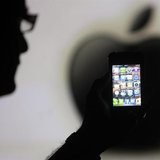 A man is silhouetted against a video screen with an Apple logo as he poses with an Apple iPhone 4 smartphone in this photo illustration take A man is silhouetted against a video screen with an Apple logo as he poses with an Apple iPhone 4 smartphone in this photo illustration take