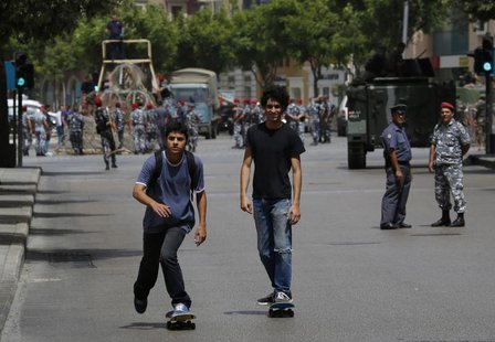 Two youths on skateboards pass by a police officer and a soldier securing a street they have closed off, where anti-Hezbollah activists had Two youths on skateboards pass by a police officer and a soldier securing a street they have closed off, where anti-Hezbollah activists had