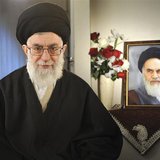 Iran's Supreme Leader Ayatollah Ali Khamenei sits next to a portrait of late leader Ayatollah Ruhollah Khomeini while taking part in a telev