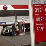 Customers fill their tanks with gasoline at an automobile service station as prices are displayed on a signboard in San Bruno, California Fe