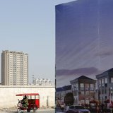 A tricycle drives past an large advertisement board of a new apartment complex at a new residential town in Beijing February 27, 2013. REUTE