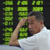 An investor looks back in front of an electronic board showing stock information filled with green-coloured figures, which indicate falling 