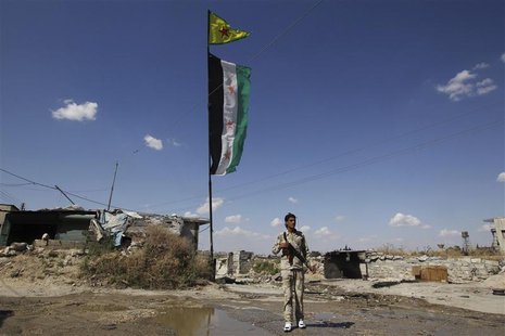 A Free Syrian Army fighter carrying his weapon, walks along a street as Syrian opposition (bottom) and Popular Protection Units (YPG) flags A Free Syrian Army fighter carrying his weapon, walks along a street as Syrian opposition (bottom) and Popular Protection Units (YPG) flags