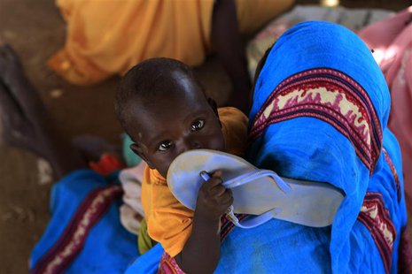 A child holds a slipper as displaced people wait at a food distribution centre as special envoys and diplomats arrive for a meeting to discu A child holds a slipper as displaced people wait at a food distribution centre as special envoys and diplomats arrive for a meeting to discu