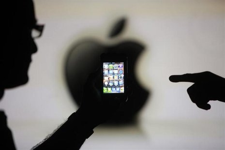 Men are silhouetted against a video screen with an Apple logo as they pose with an Apple iPhone 4 smartphone in this photo illustration take Men are silhouetted against a video screen with an Apple logo as they pose with an Apple iPhone 4 smartphone in this photo illustration take