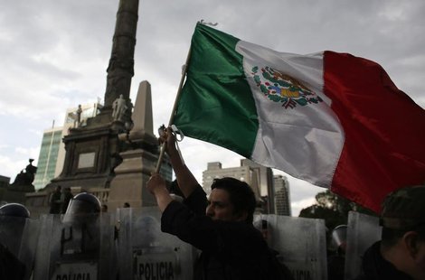 A demonstrator holds a Mexican national flag in front of riot policemen during a protest against the privatization of the state oil monopoly A demonstrator holds a Mexican national flag in front of riot policemen during a protest against the privatization of the state oil monopoly