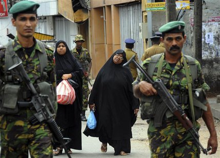 Two Muslim women walk behind patrolling Special Task Force Commandos outside a vandalized mosque in Colombo August 11, 2013. REUTERS/Stringe Two Muslim women walk behind patrolling Special Task Force Commandos outside a vandalized mosque in Colombo August 11, 2013. REUTERS/Stringe