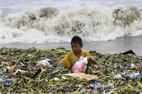 A boy sifts through floating garbage as he collects recyclable items to sell while strong waves crash along the shores of Manila Bay, near a A boy sifts through floating garbage as he collects recyclable items to sell while strong waves crash along the shores of Manila Bay, near a