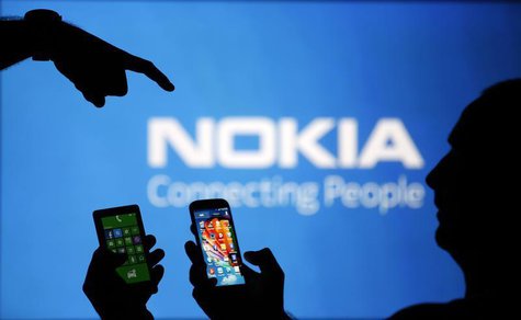 Men are silhouetted against a video screen with an Nokia logo as he poses with an Nokia Lumia 820 and Samsung S4 smartphones in this photo i Men are silhouetted against a video screen with an Nokia logo as he poses with an Nokia Lumia 820 and Samsung S4 smartphones in this photo i