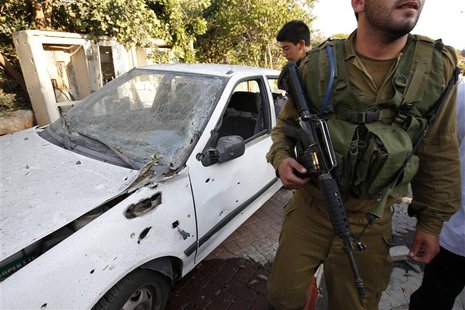 An Israeli soldier walks past a car damaged by a barrage of Lebanese rockets fired at Israel, in Kibbutz Gesher HaZiv, near the northern cit An Israeli soldier walks past a car damaged by a barrage of Lebanese rockets fired at Israel, in Kibbutz Gesher HaZiv, near the northern cit