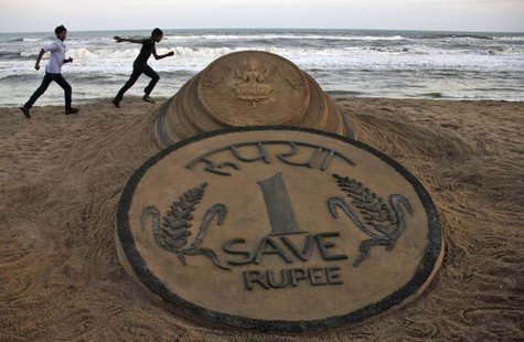 Boys run near a sand sculpture of the Indian Rupee created by Indian sand artist Sudarshan Pattnaik at golden sea beach at Puri in the easte Boys run near a sand sculpture of the Indian Rupee created by Indian sand artist Sudarshan Pattnaik at golden sea beach at Puri in the easte