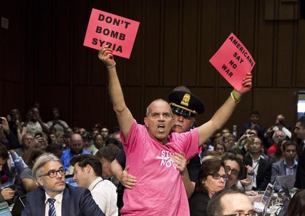 A protester waves signs as Chairman of the Joint Chiefs General Martin E. Dempsey, John Kerry, U.S. Secretary of State, and Chuck Hagel, Sec A protester waves signs as Chairman of the Joint Chiefs General Martin E. Dempsey, John Kerry, U.S. Secretary of State, and Chuck Hagel, Sec