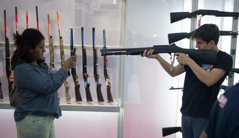 A woman uses a smart phone to photograph a young man holding a shotgun at an exhibit booth at the George R. Brown convention center, the sit A woman uses a smart phone to photograph a young man holding a shotgun at an exhibit booth at the George R. Brown convention center, the sit
