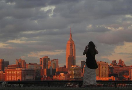 A woman stops to photograph the skyline of New York across from the Empire State Building as she walks in a park along the Hudson River in H A woman stops to photograph the skyline of New York across from the Empire State Building as she walks in a park along the Hudson River in H