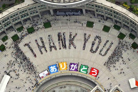An aerial view shows people sitting in formation to the words "thank you" and displaying signs that collectively read "Arigato" (Thank You) An aerial view shows people sitting in formation to the words "thank you" and displaying signs that collectively read "Arigato" (Thank You)