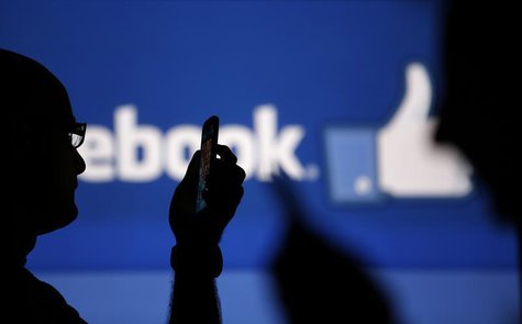 Men are silhouetted against a video screen with an Facebook logo as he poses with an Nokia Lumia 820 and Samsung Galaxy S4 in this photo ill Men are silhouetted against a video screen with an Facebook logo as he poses with an Nokia Lumia 820 and Samsung Galaxy S4 in this photo ill