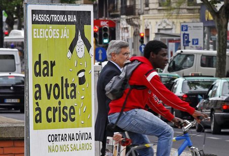 People pass by a political poster reading, "Passos/Toika out. Elections now. Turn the crisis around. Cut the debt and not the salaries", on People pass by a political poster reading, "Passos/Toika out. Elections now. Turn the crisis around. Cut the debt and not the salaries", on