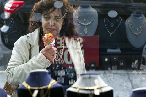 A woman eats ice cream as she looks at the display in the window of a Gold Standard jewellery store that specializes in purchasing raw gold A woman eats ice cream as she looks at the display in the window of a Gold Standard jewellery store that specializes in purchasing raw gold