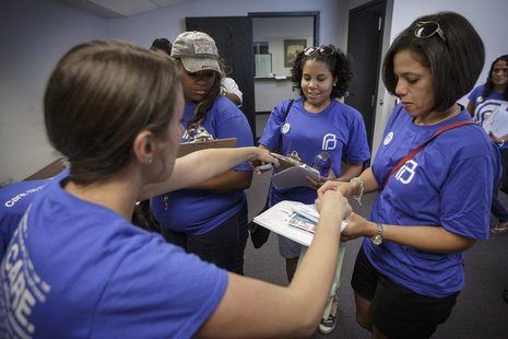 Get Covered America volunteers Cynae Derose (2nd R) and Jalisa Hinkle (3nd R) pick up their supplies from Allyson Raines before knocking on Get Covered America volunteers Cynae Derose (2nd R) and Jalisa Hinkle (3nd R) pick up their supplies from Allyson Raines before knocking on