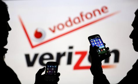 Men are silhouetted against a video screen with Vodafone and Verizon texts as they pose with Blackberry Q10 and Samsung Galaxy S3 in this ph Men are silhouetted against a video screen with Vodafone and Verizon texts as they pose with Blackberry Q10 and Samsung Galaxy S3 in this ph
