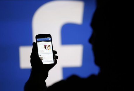 A man is silhouetted against a video screen with an Facebook logo as he poses with an Samsung S4 smartphone in this photo illustration taken A man is silhouetted against a video screen with an Facebook logo as he poses with an Samsung S4 smartphone in this photo illustration taken