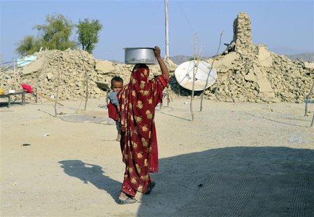 A survivor of an earthquake carries a pot on her head filled with drinking water as she walks near the rubble of a mud house after it collap A survivor of an earthquake carries a pot on her head filled with drinking water as she walks near the rubble of a mud house after it collap