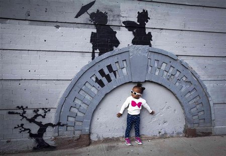 A child poses for a photo under a new art piece by British graffiti artist Banksy in the Brooklyn borough of New York, October 17, 2013. REU A child poses for a photo under a new art piece by British graffiti artist Banksy in the Brooklyn borough of New York, October 17, 2013. REU