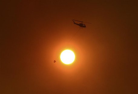A helicopter with a bucket used for carrying water for dropping onto bushfires, flies past the sun as it is obscured by smoke in western Syd A helicopter with a bucket used for carrying water for dropping onto bushfires, flies past the sun as it is obscured by smoke in western Syd