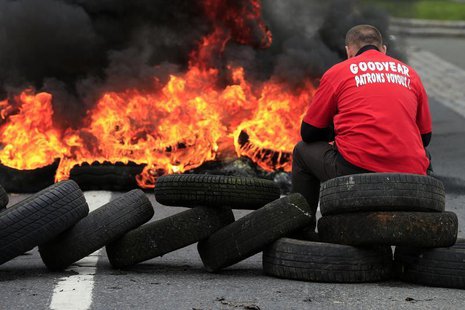 Flames and smoke rise from burning tyres as a worker sits on a barricade blocking the entrance of U.S. tyre-maker Goodyear's plant to protes Flames and smoke rise from burning tyres as a worker sits on a barricade blocking the entrance of U.S. tyre-maker Goodyear's plant to protes