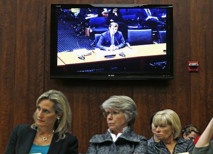 Audience members listen to Illinois Assistant Attorney General and Director of Public Policy Erik Jones (on screen) testify at an Illinois H Audience members listen to Illinois Assistant Attorney General and Director of Public Policy Erik Jones (on screen) testify at an Illinois H