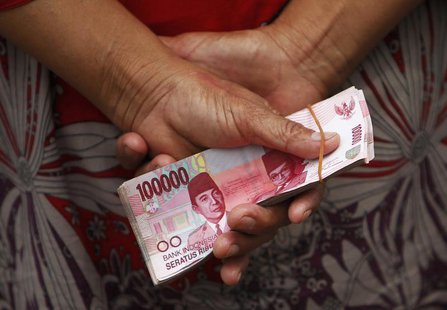 A woman holds Indonesian rupiah banknotes in front of a Bank Indonesia mobile bank in Jakarta July 15, 2013. REUTERS/Beawiharta A woman holds Indonesian rupiah banknotes in front of a Bank Indonesia mobile bank in Jakarta July 15, 2013. REUTERS/Beawiharta