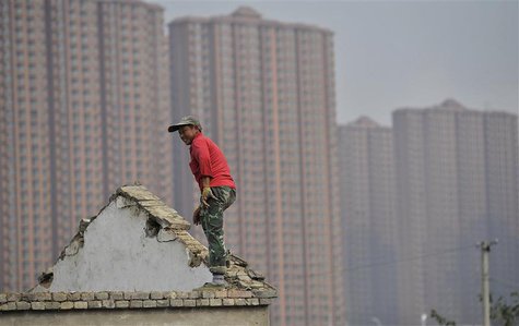A man stands on the top of a building as farmers' houses are demolished to make space for new property to be built, in front of a residentia A man stands on the top of a building as farmers' houses are demolished to make space for new property to be built, in front of a residentia