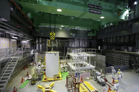 Workers wearing protective suits and masks work on a crane for a transport container inside the No. 4 reactor building at the tsunami-crippl Workers wearing protective suits and masks work on a crane for a transport container inside the No. 4 reactor building at the tsunami-crippl