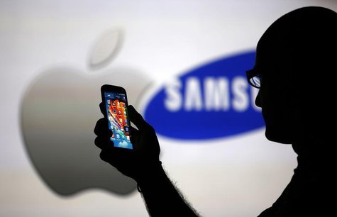 A man is silhouetted against a video screen with Apple and Samsung logos as he poses with a Samsung Galaxy S4 in this photo illustration tak A man is silhouetted against a video screen with Apple and Samsung logos as he poses with a Samsung Galaxy S4 in this photo illustration tak
