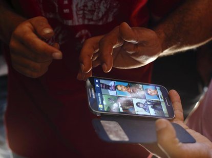Syrian refugees look at photos of their missing and believed to have drowned compatriots on a smartphone, at the Hal Far open centre for mig Syrian refugees look at photos of their missing and believed to have drowned compatriots on a smartphone, at the Hal Far open centre for mig