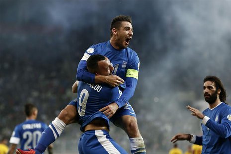 Greece's Kostas Katsouranis (top) jumps onto Kostas Mitroglou as they celebrate Mitroglou's goal against Romania during their 2014 World Cup Greece's Kostas Katsouranis (top) jumps onto Kostas Mitroglou as they celebrate Mitroglou's goal against Romania during their 2014 World Cup