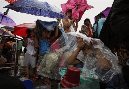 Residents shelter from the rain as they wait to get onto a military plane during an evacuation at Tacloban airport in the Typhoon Haiyan dev Residents shelter from the rain as they wait to get onto a military plane during an evacuation at Tacloban airport in the Typhoon Haiyan dev