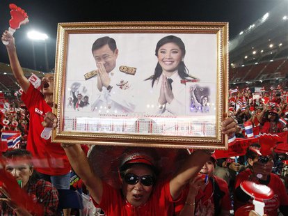 A red-shirted supporter holds up a pictures of Thailand's Prime Minister Yingluck Shinawatra and her brother Thaksin Shinawatra, during a ra A red-shirted supporter holds up a pictures of Thailand's Prime Minister Yingluck Shinawatra and her brother Thaksin Shinawatra, during a ra