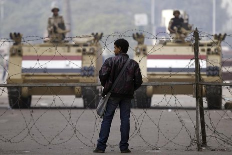 A man stands in front of a barbed wire fence set up by soldiers standing guard on armoured personnel carriers (APC) on Mohamed Mahmoud Stree A man stands in front of a barbed wire fence set up by soldiers standing guard on armoured personnel carriers (APC) on Mohamed Mahmoud Stree