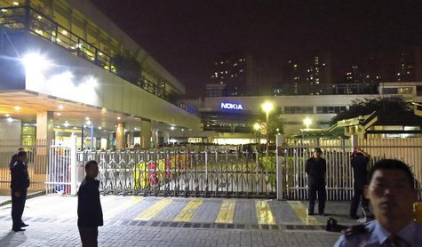 Police and security guards stand outside a gate of a Nokia factory during a protest of around one hundred factory workers in Dongguan, Guang Police and security guards stand outside a gate of a Nokia factory during a protest of around one hundred factory workers in Dongguan, Guang