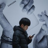 A passenger using his mobile phone walks past an advertisement promoting Samsung Electronics' Galaxy Note 3 at its exhibition hall at a rail A passenger using his mobile phone walks past an advertisement promoting Samsung Electronics' Galaxy Note 3 at its exhibition hall at a rail