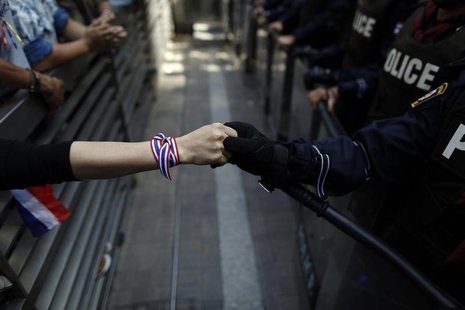 An anti-government protester holds hands with an anti-riot policemen across the closed gates outside the headquarters of the ruling Puea Tha An anti-government protester holds hands with an anti-riot policemen across the closed gates outside the headquarters of the ruling Puea Tha