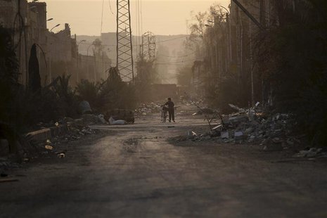 A resident walks his bicycle through damage and debris on a street Deir al-Zor, eastern Syria November 29, 2013.Picture taken November 29, 2 A resident walks his bicycle through damage and debris on a street Deir al-Zor, eastern Syria November 29, 2013.Picture taken November 29, 2