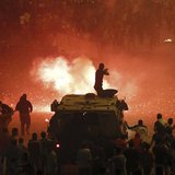 A riot police officer, on a armoured personnel carrier surrounded by anti-Mursi protesters (foreground), fires rubber bullets at members of A riot police officer, on a armoured personnel carrier surrounded by anti-Mursi protesters (foreground), fires rubber bullets at members of
